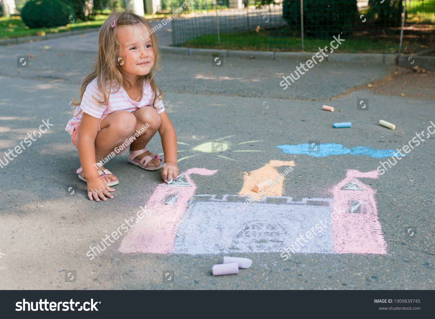 Girl drawing castle with colored chalks on the sidewalk near the house on sunny summer day. Kids painting outside. Creative development of children. #1909839745