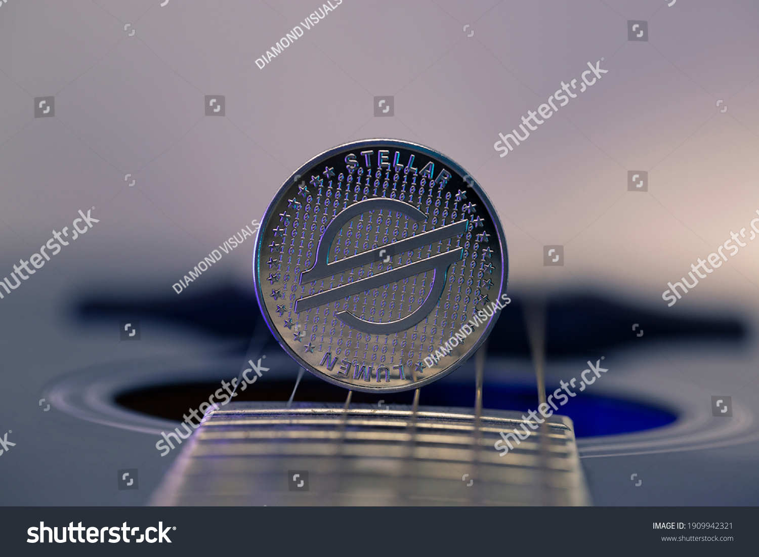 Stellar Lumens XLM cryptocurrency physical coin placed on guitar strings and lit with blue light. Macro shot. #1909942321