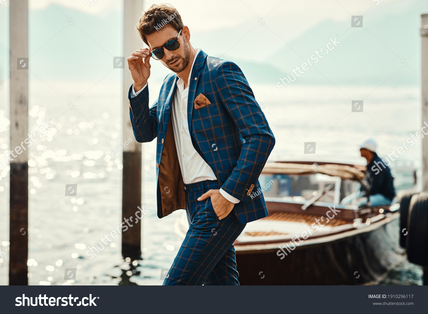 Young handsome man in classic suit wear sunglasses over the blurred lake  #1910296117