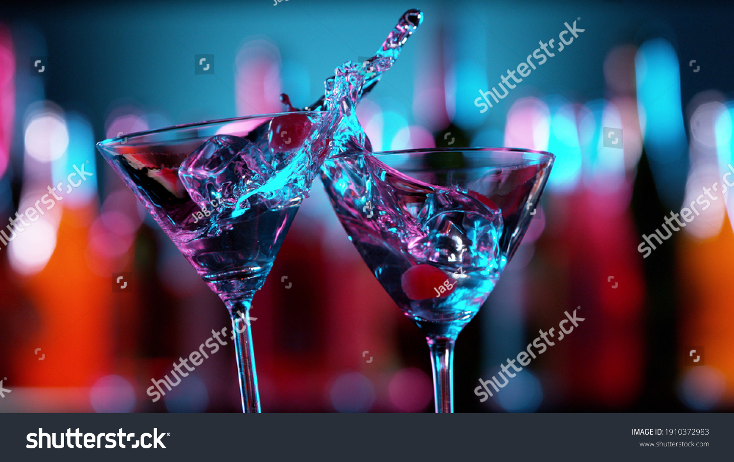 Closeup of splashing martini cocktails in cheers gesture. Bar on background, free space for text #1910372983