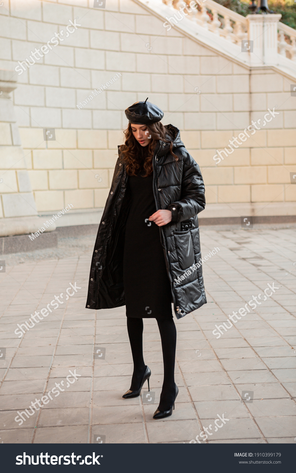 stylish woman posing in winter autumn fashion trend black puffer coat and leather hat beret in old beautiful street wearing high heel shoes #1910399179