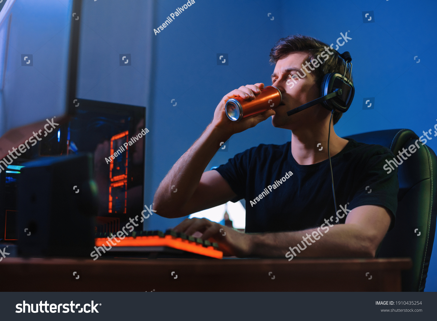 Cyber sport. Professional cybersport player training or playing online video game on his PC late at night, drinking caffeine energy drink to concentrate, focus on game. Team play. Games addiction #1910435254