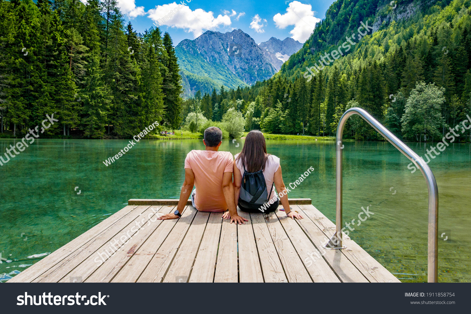 Rear view of young female sitting on wooden deck by beautiful lake in mountains  Green, spring, flower crown, outdoors  Zgornje Jezersko, Slovenia #1911858754