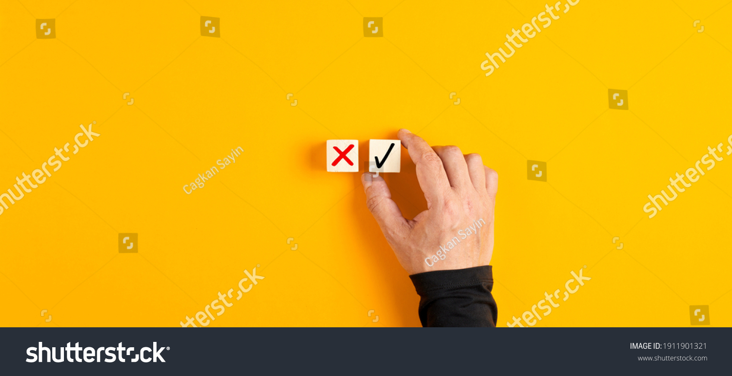 Right and wrong icons on wooden cubes with male hand choosing the right icon on yellow background. Approving, voting or right decision concept.

 #1911901321