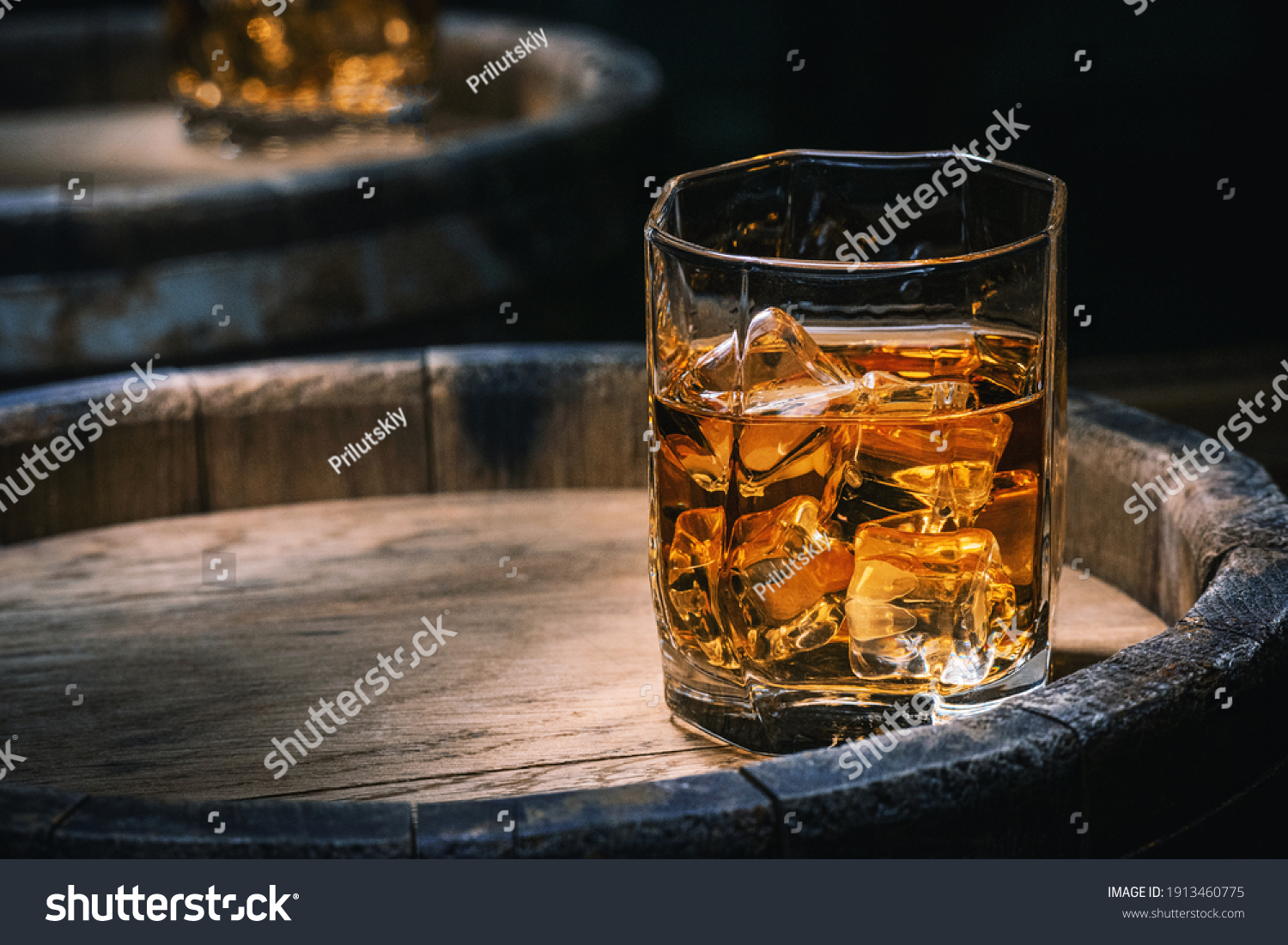 Bottle and glass of whiskey with ice on a wooden background. Glass of Scotch whiskey and ice sits on top of a rustic whiskey barrel. Whiskey with ice. #1913460775