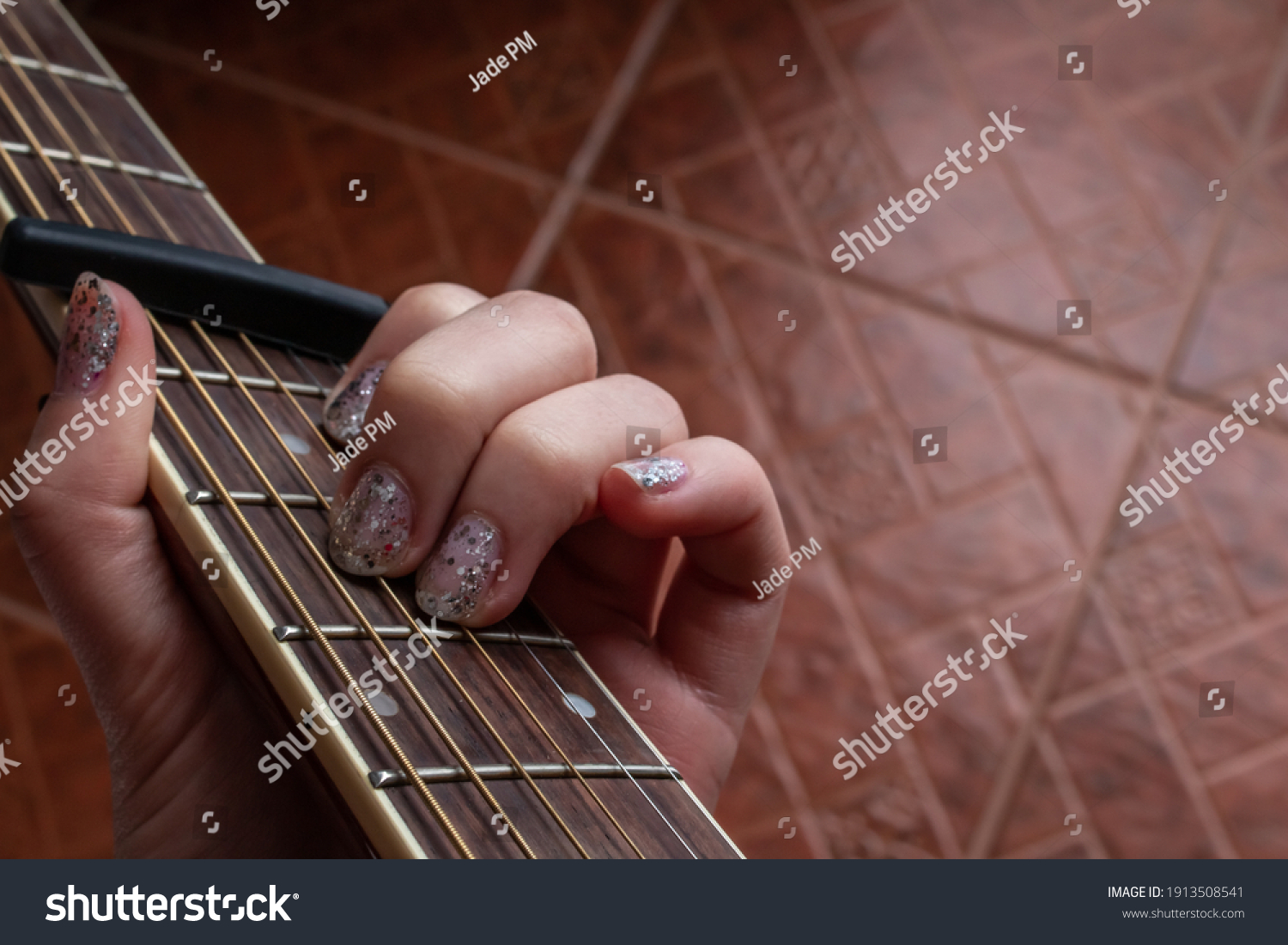 A woman with glitter nail polish plays an A minor chord on an accoustic guitar, fitted with a capo, February 2021 during COVID-19 lockdowns. #1913508541