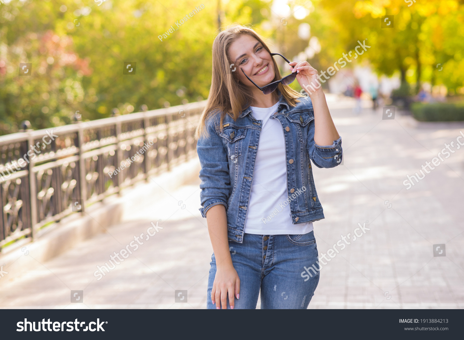 Portrait of a happy and attractive blonde Caucasian young woman in a casual denim jacket outdoors in a park on a sunny autumn day. A concept of lifestyle, happiness and joy. #1913884213