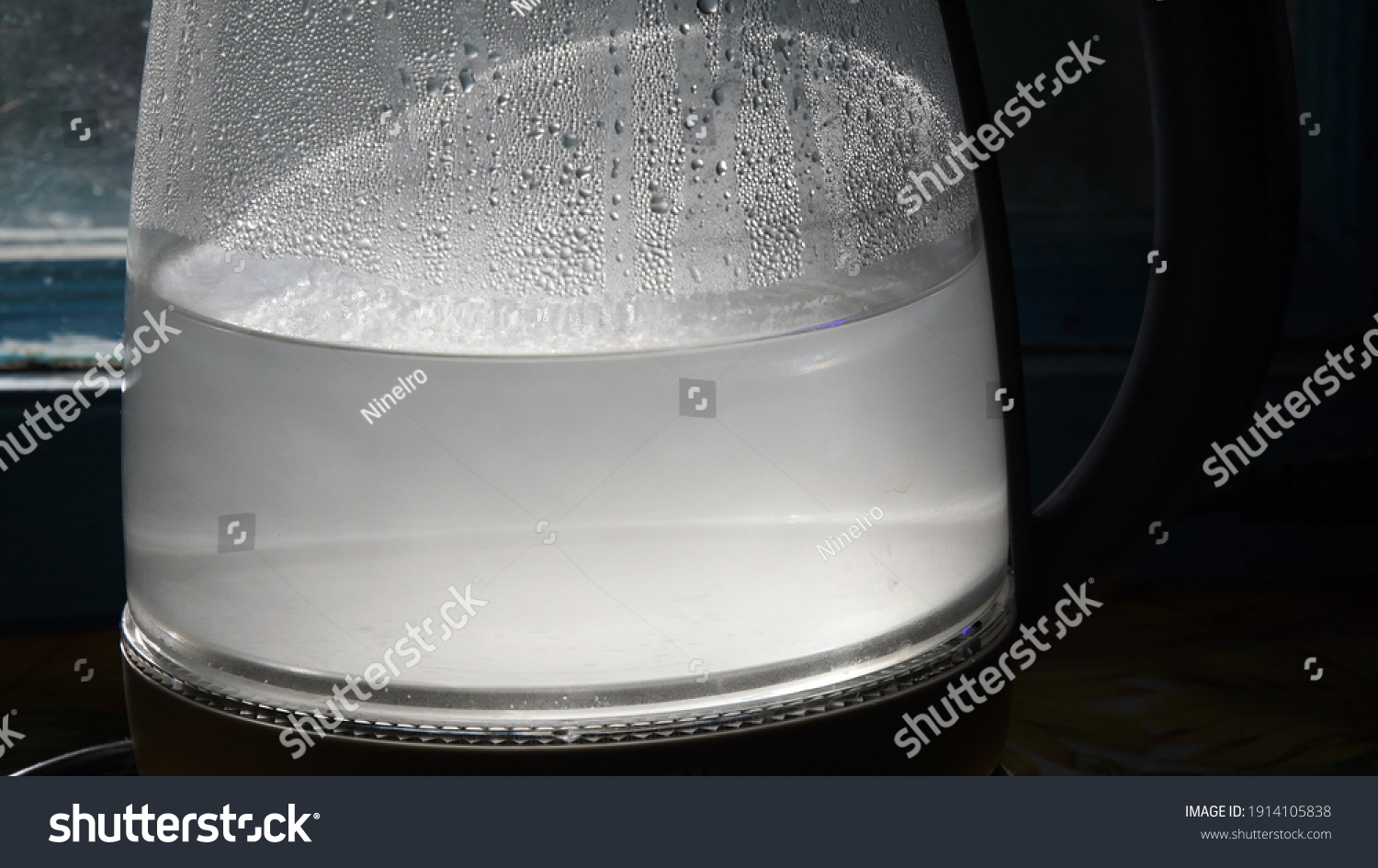 Turbid water inside misted glass teapot with shiny drops in bright sunlight. Closeup of boiled water in old transparent kettle on kitchen #1914105838