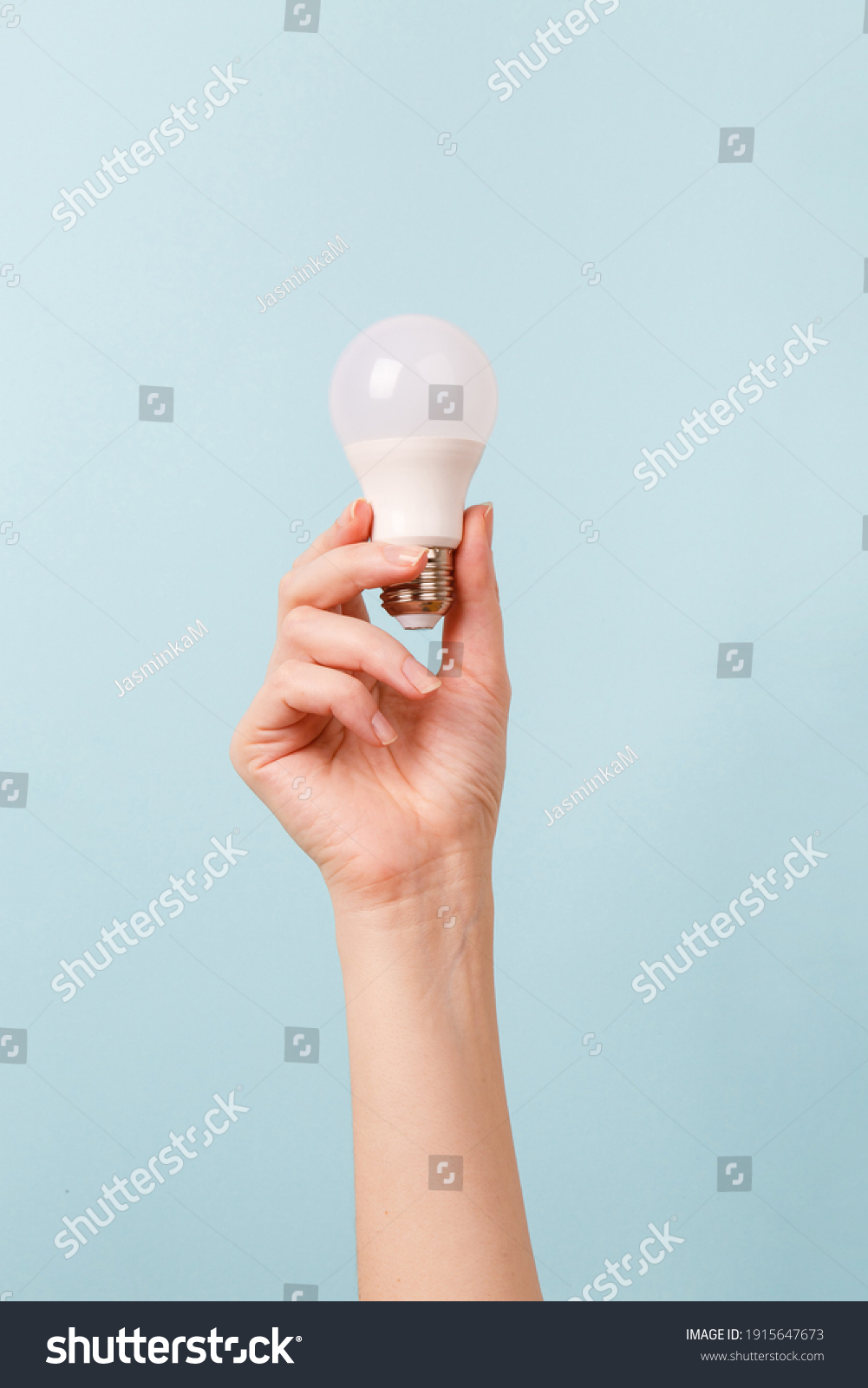 Hand holding a LED light bulb on blue background. Using economical and environmentally friendly light bulb concept. Idea. Energy saving lamp in woman's hand #1915647673