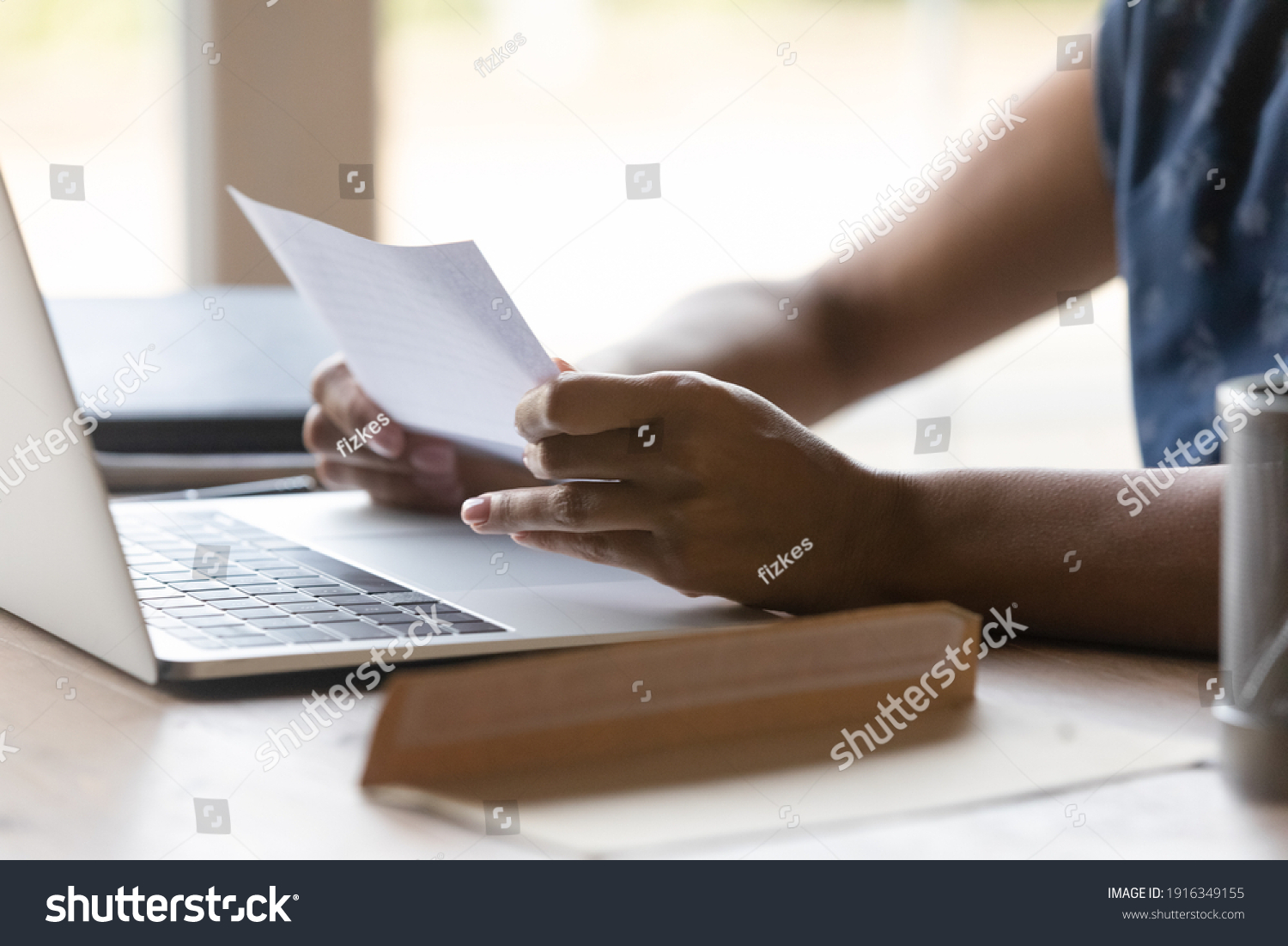 Close up African American woman reading letter at home, sitting at table with open envelope and laptop, businesswoman working with correspondence, received information from bank or college #1916349155