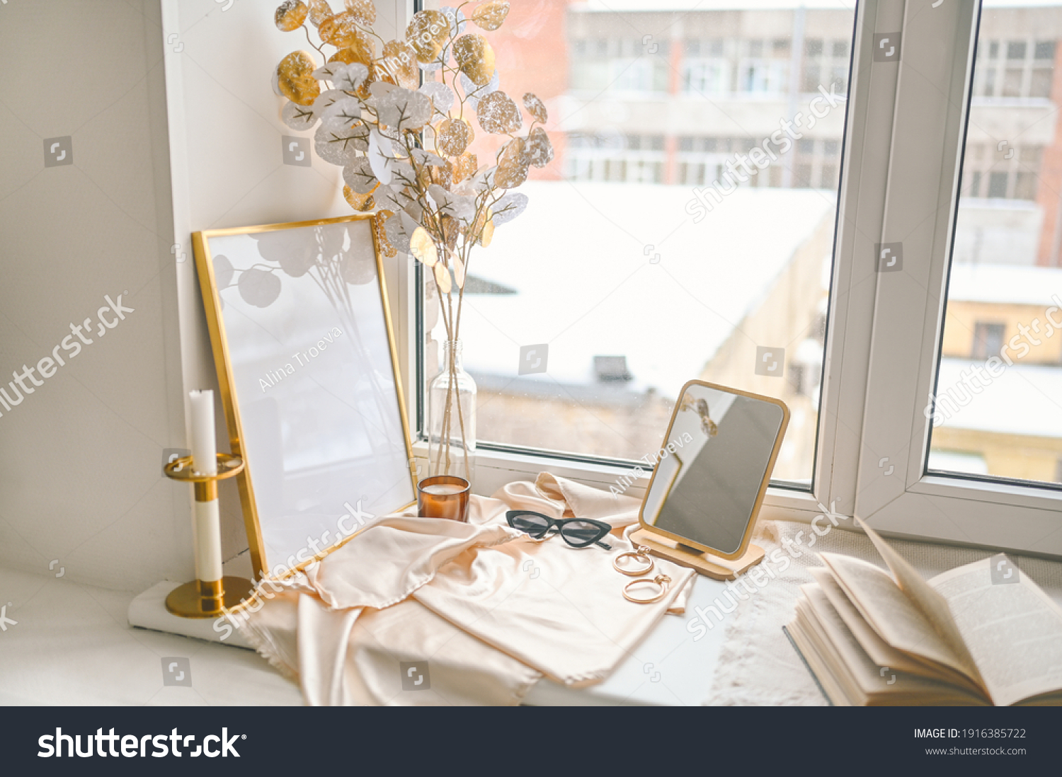 Cozy spring still life feminine scene golden shades. Female styled window sill minimalistic composition. Empty picture mock up poster frame, elegant accessories mirror earrings, dried flowers, candle #1916385722