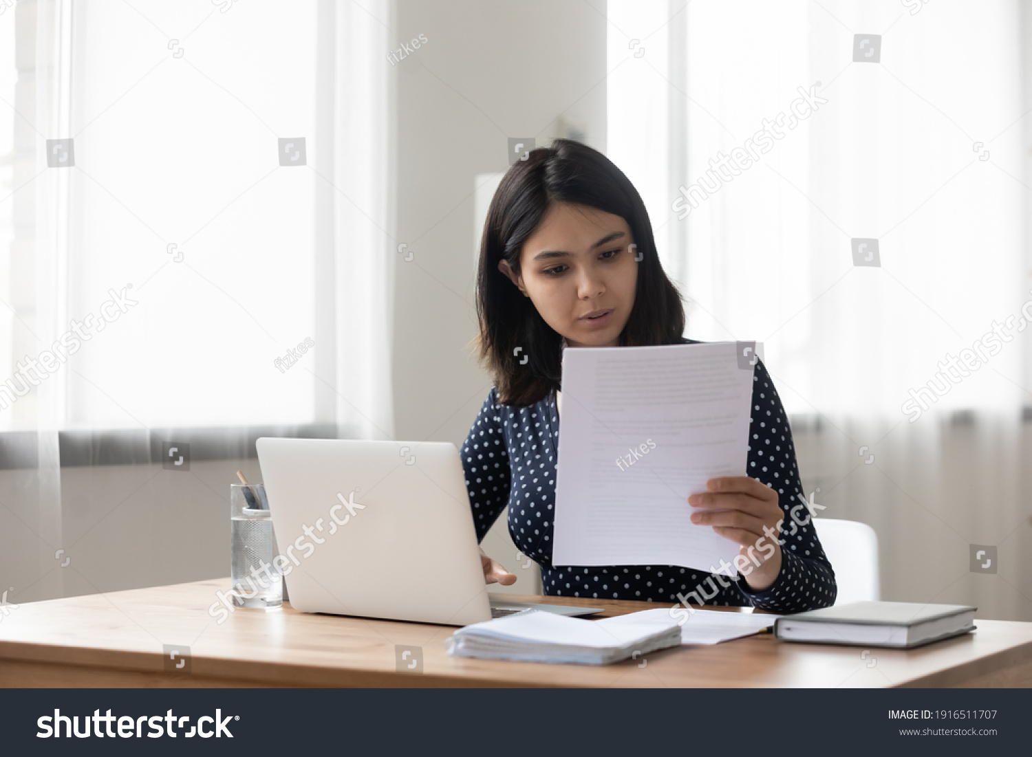Attentive millennial asian female holding paper letter document reading financial statement. Focused vietnamese business woman worker employee review offer proposal study job contract terms conditions #1916511707
