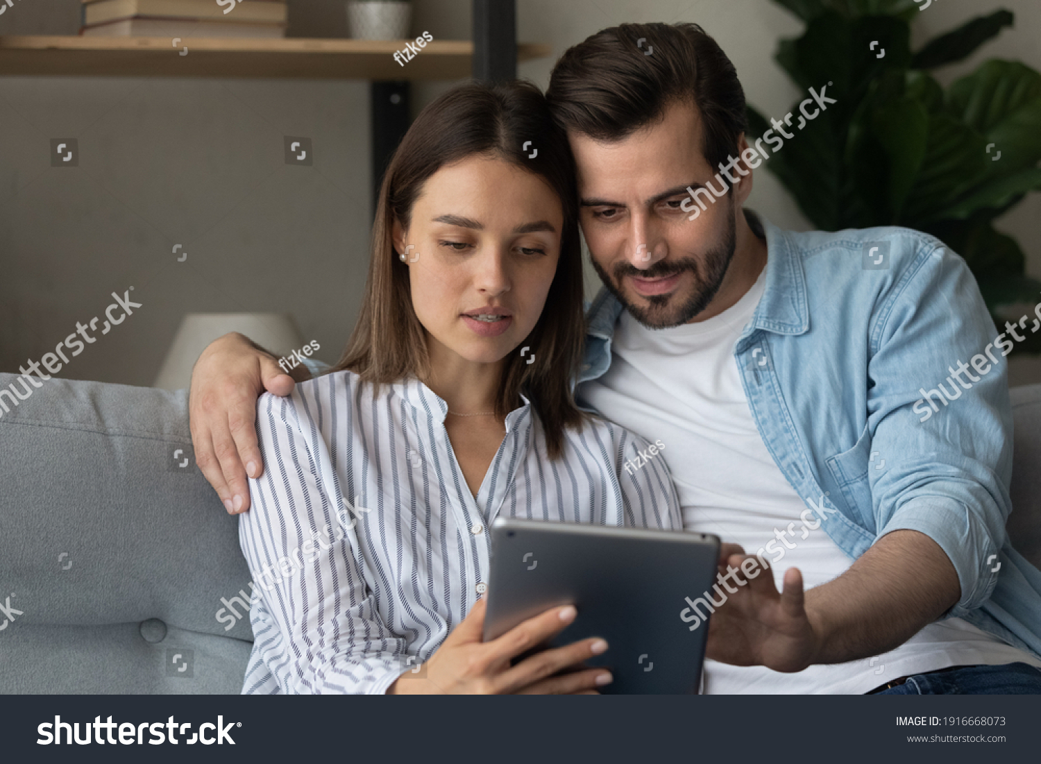 Focused married couple read insurance policy loan contract text from bank website on tablet screen planning to make treaty. Serious young spouses hold digital pad device buy goods order service online #1916668073