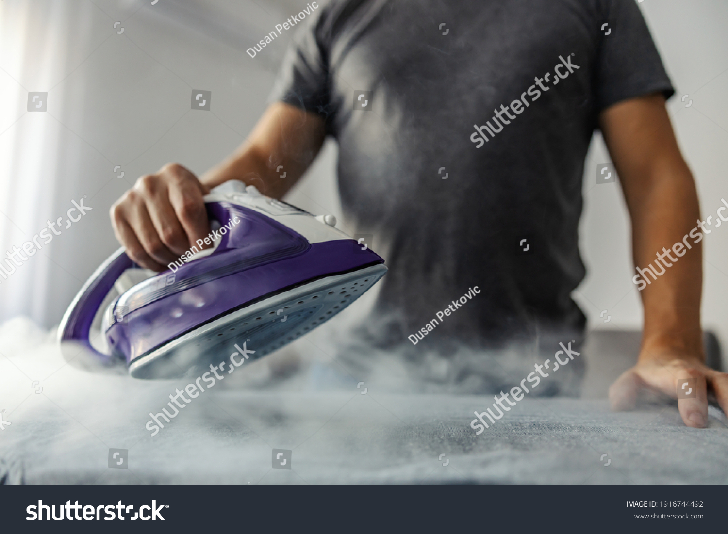 Powerful professional photo effect of water vapor from the hot iron. A modern lifestyle concept, a man who irons clothes at home #1916744492