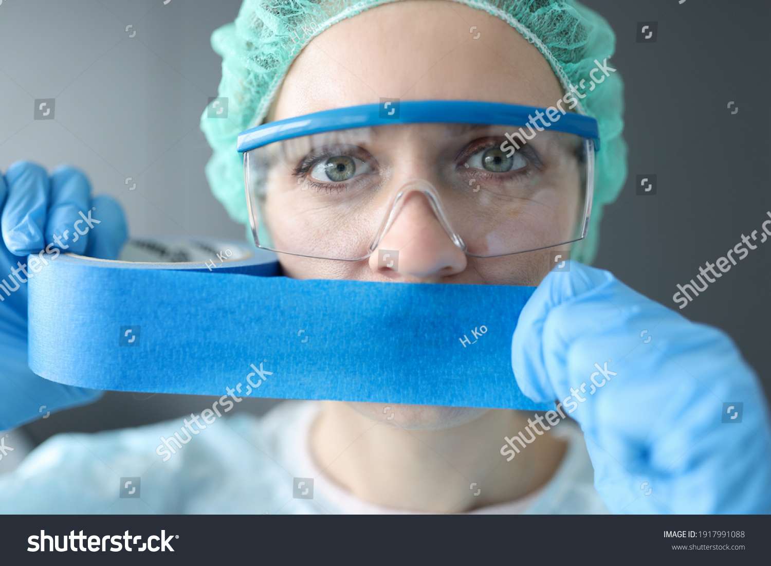 Woman doctor sealing her mouth with blue tape. Medical secrecy concept #1917991088