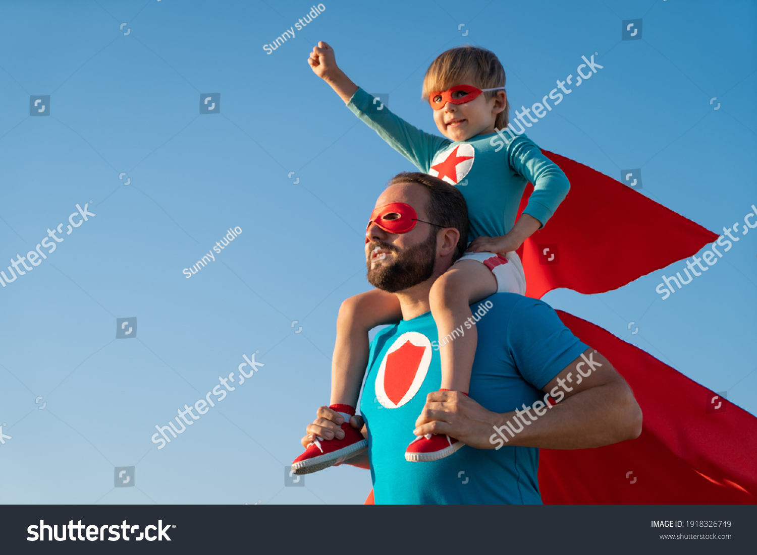 Family of superheroes having fun outdoor. Father and son playing against blue summer sky background. Imagination and freedom concept #1918326749