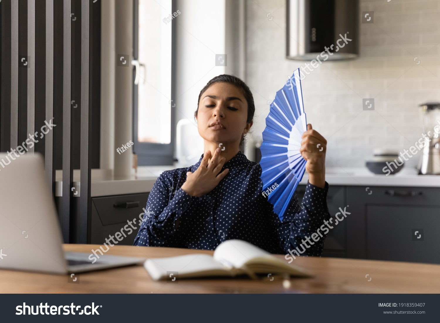 Unwell millennial Indian woman work on laptop at home office wave with hand fan feel overheated. Unhealthy tired young ethnic female use waver, suffer from hot weather or lack of AC indoors. #1918359407