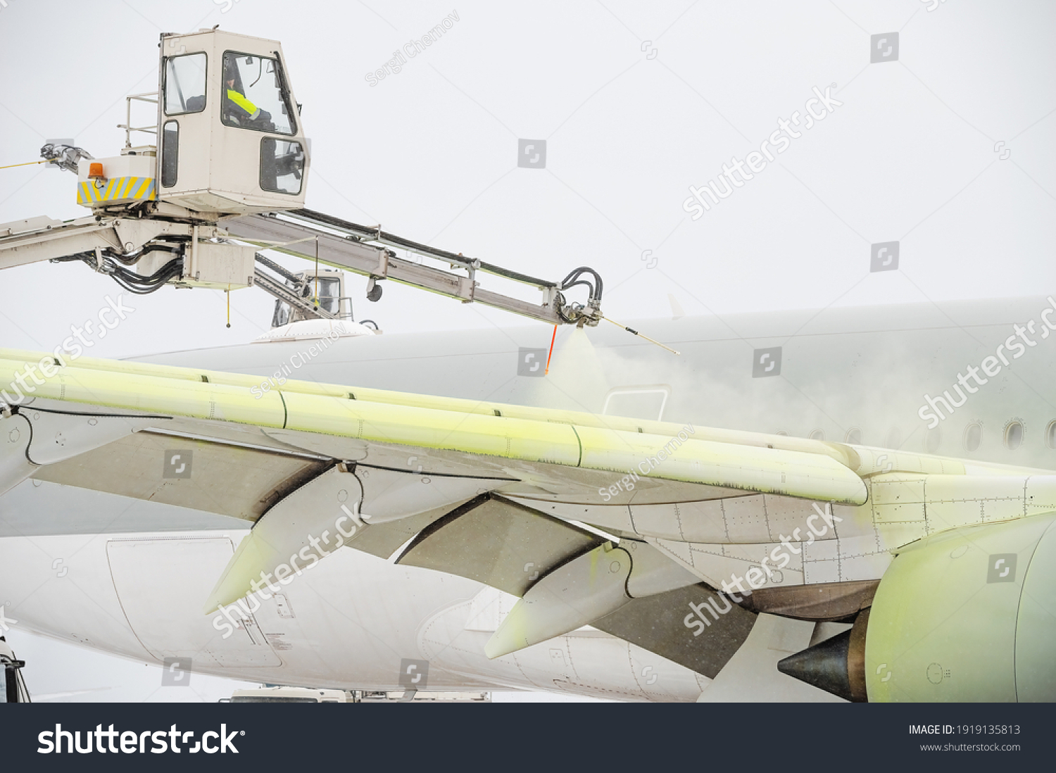 Winter at the airport. Snow storm. Airplane de-icing before take off. De-icing the aircraft before the flight. The de-icing machine sprinkles the wing of a passenger plane with de-icing fluid. #1919135813
