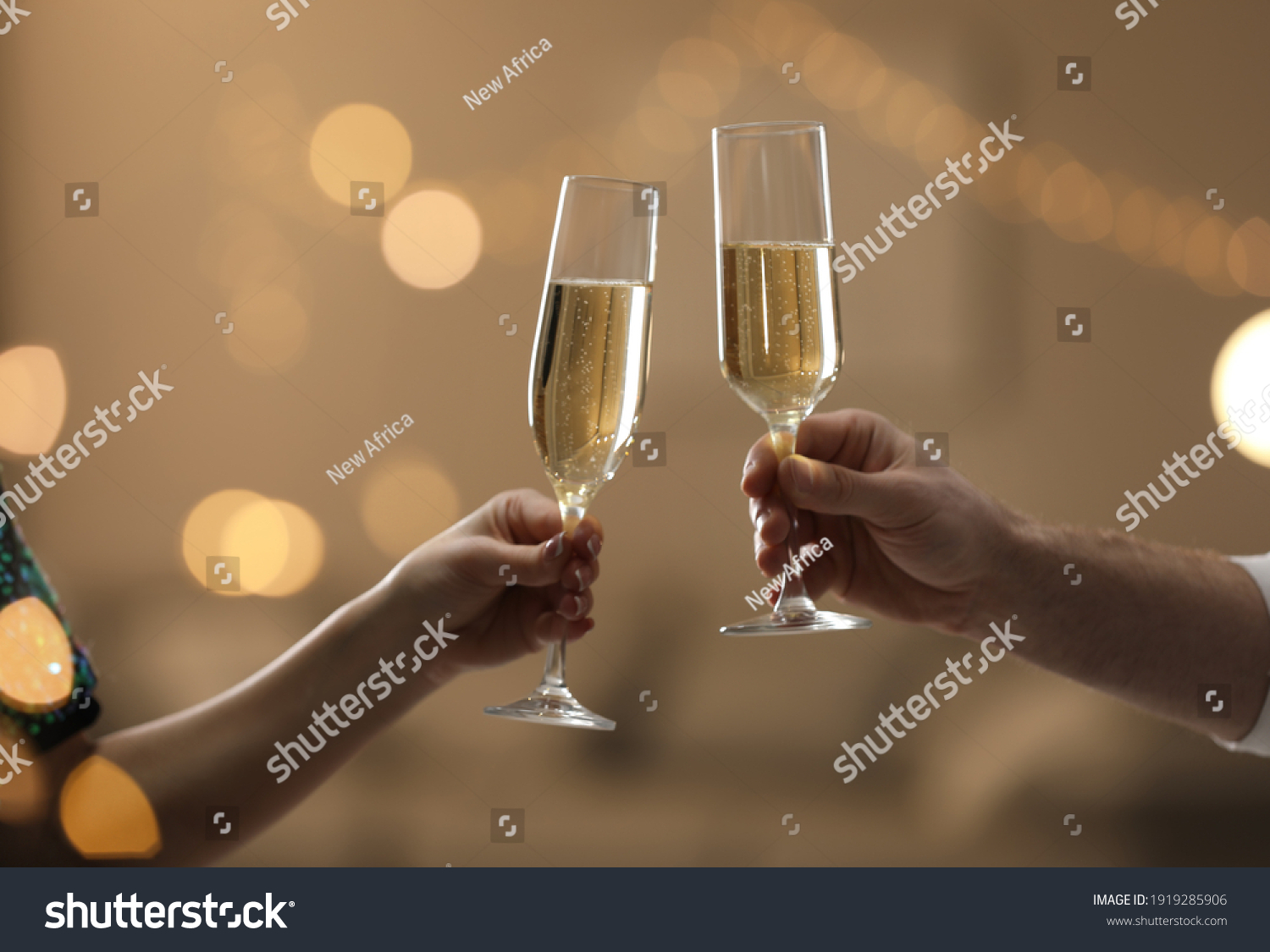 People clinking glasses of champagne against blurred background, closeup. Bokeh effect #1919285906