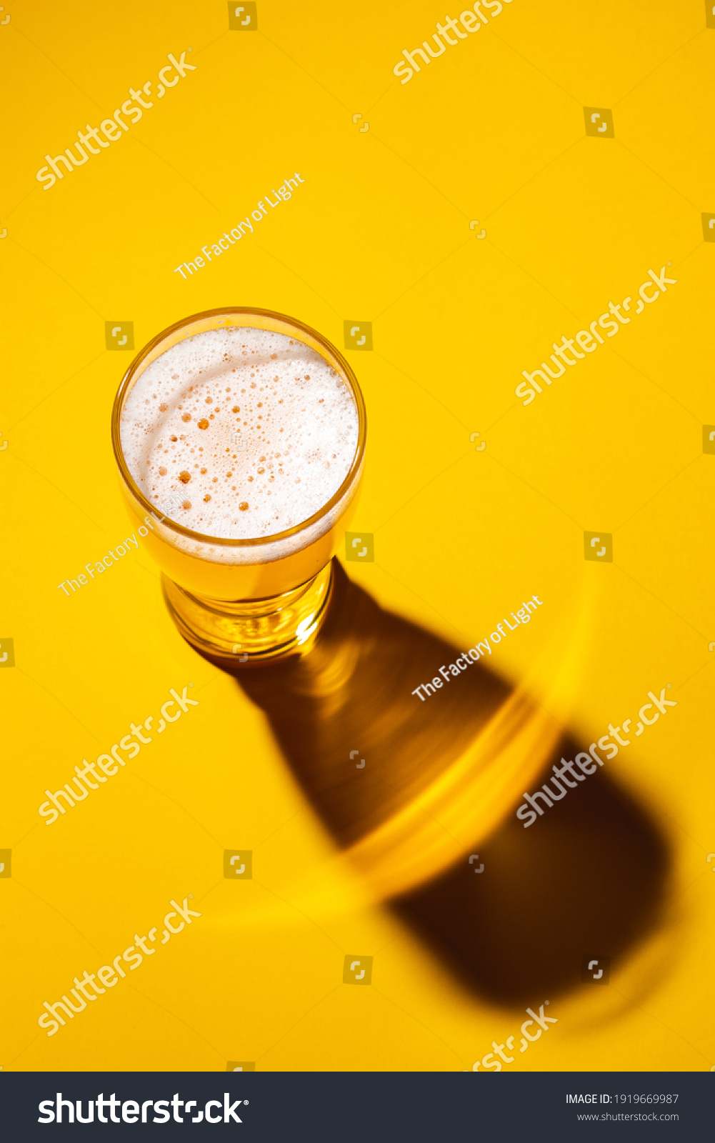 Glass of light beer on a yellow background, top view. Shadow from a glass of lager.  #1919669987