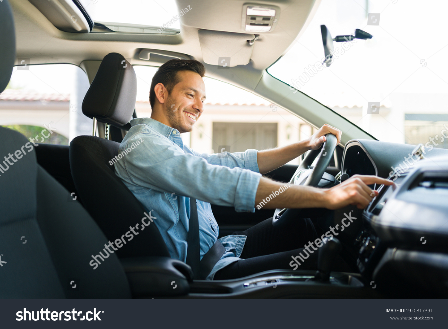 Handsome man in his 30s sitting in the driver's seat and smiling. Taxi driver listening to music on the car and changing the radio station #1920817391