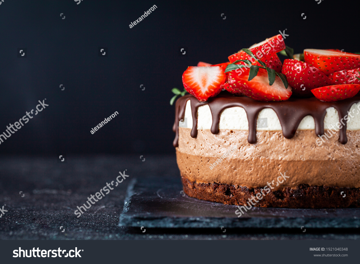 Three chocolates cake with chocolate drips on a black background. Layered cake with milk, black and white chocolate souffle decorated with strawberries on top. Confectionery background with copy space #1921040348