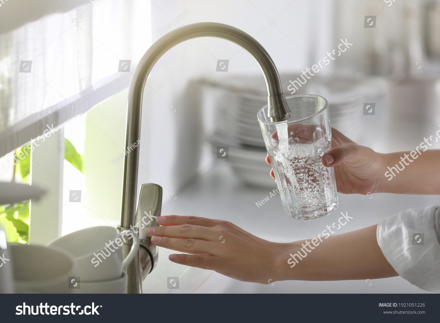 Woman pouring water into glass in kitchen, closeup #1921051226