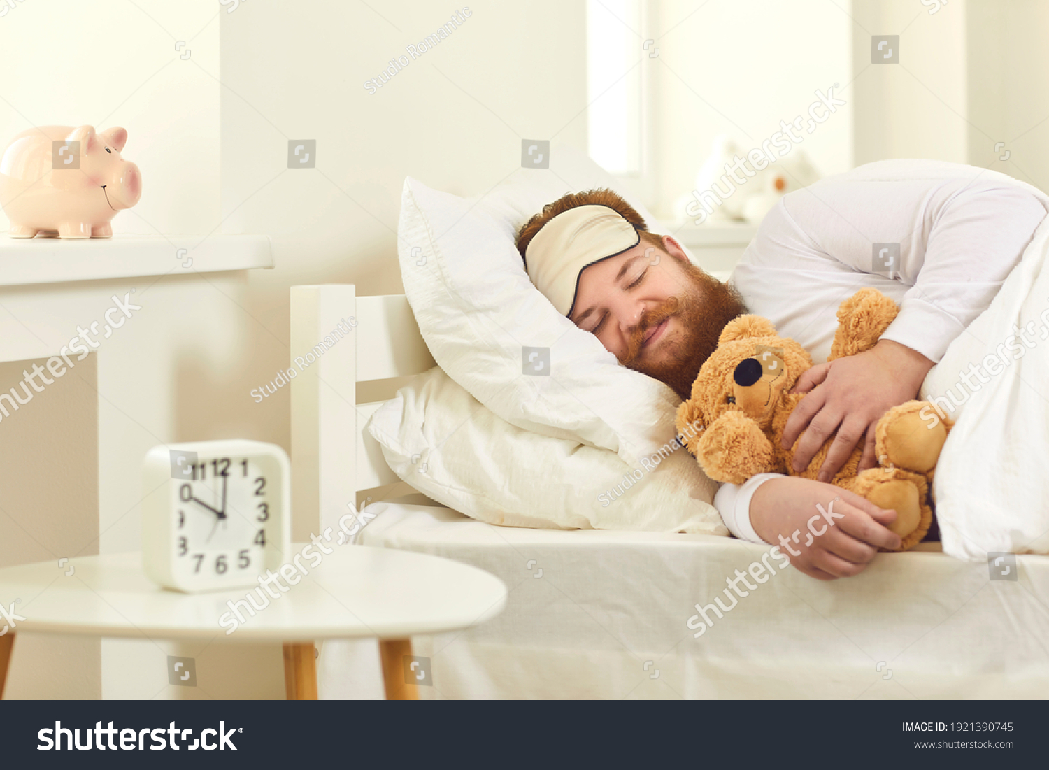 Happy grown-up man sleeping in good comfortable bed with cute teddy bear. Funny guy lying on white pillows and dreaming sweet dreams in deep sleep at 10 am in Covid-19 lockdown or on weekend morning #1921390745