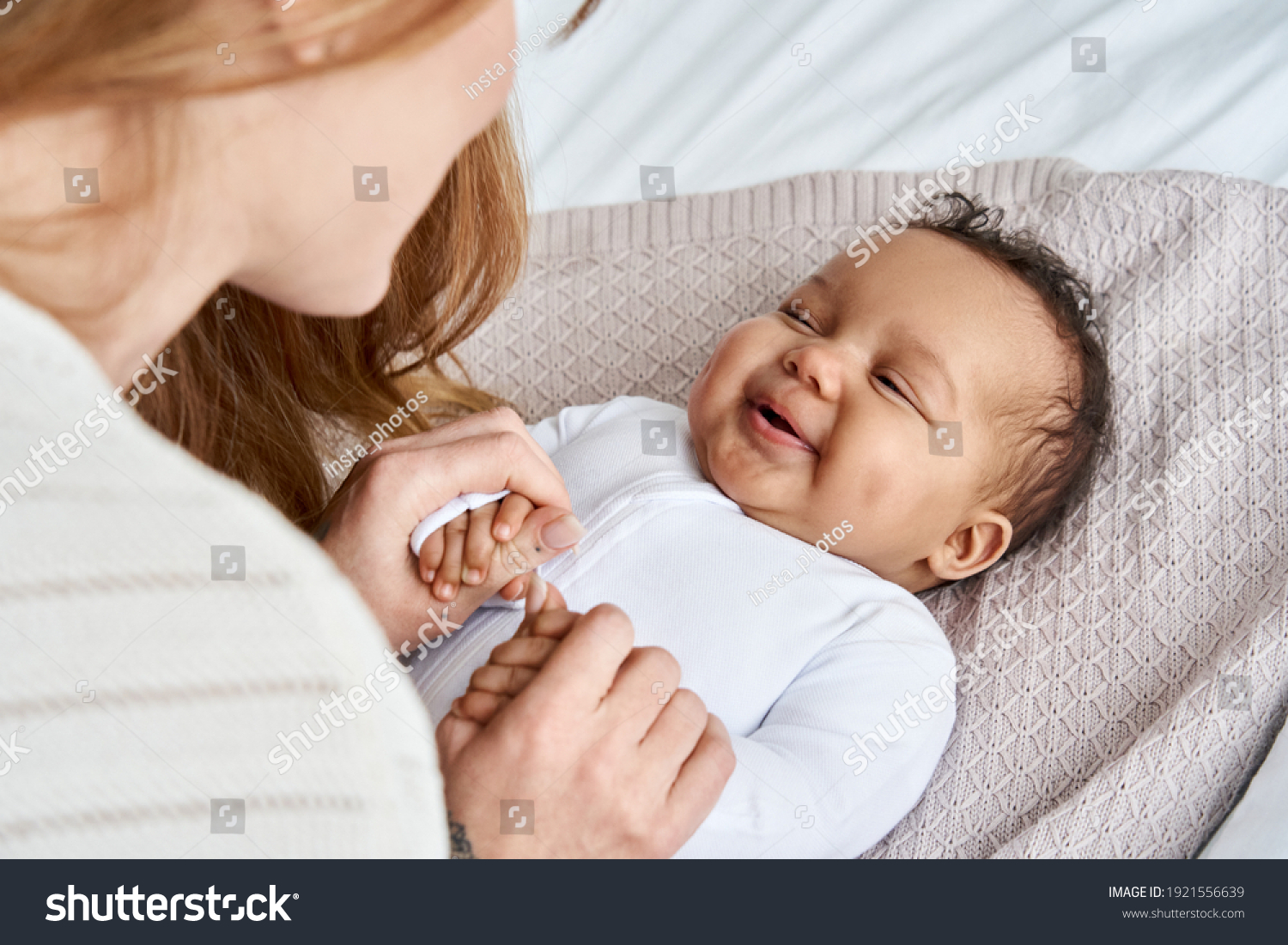 Caucasian mum, foster single parent holding hands of happy cute adorable adopted infant african american baby girl daughter lying on bed. Child care, diverse ethnicity mother and child concept. #1921556639