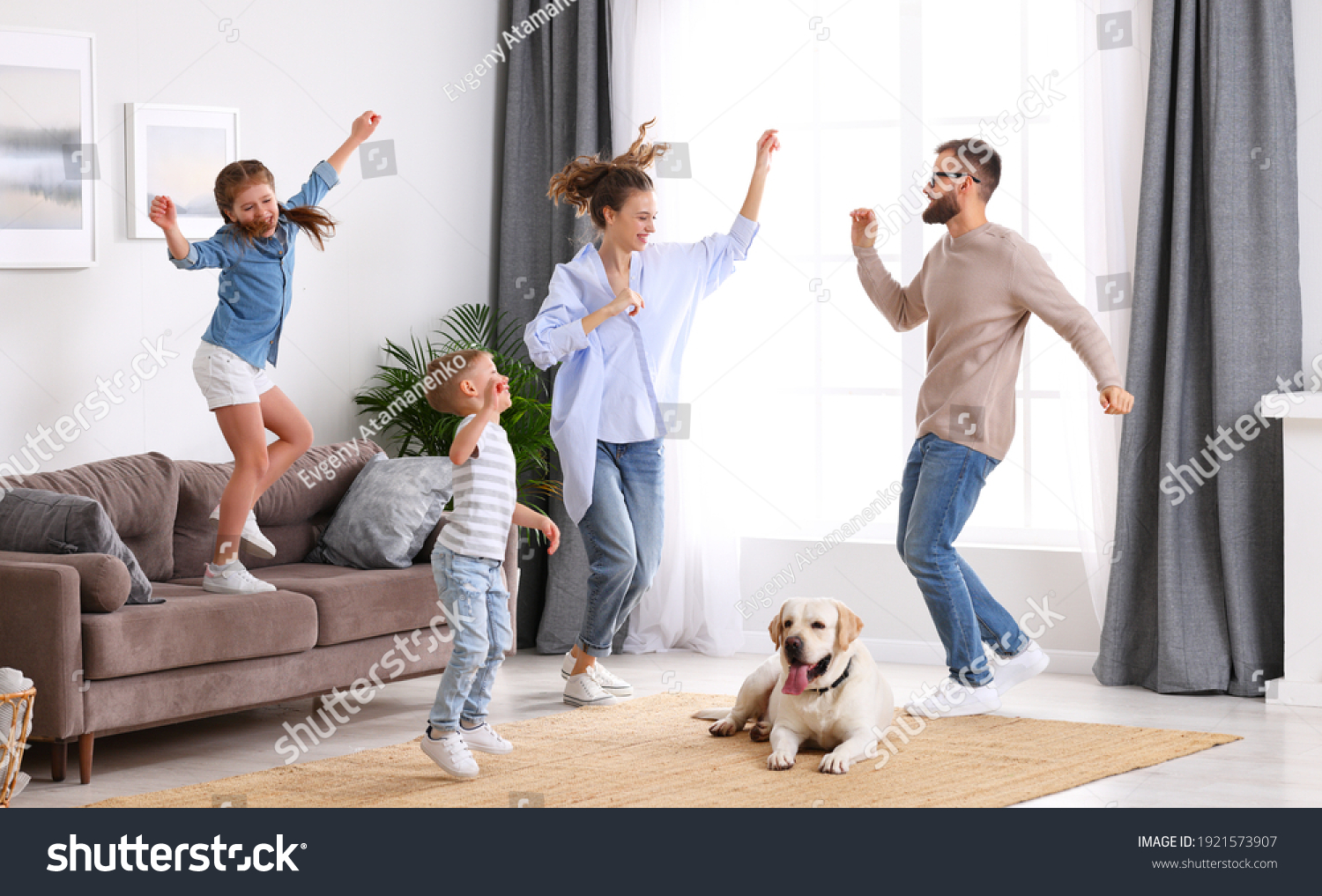 Full body of happy energetic family: parents and kids having fun and dancing while cute tired dog resting on carpet during weekend at home #1921573907