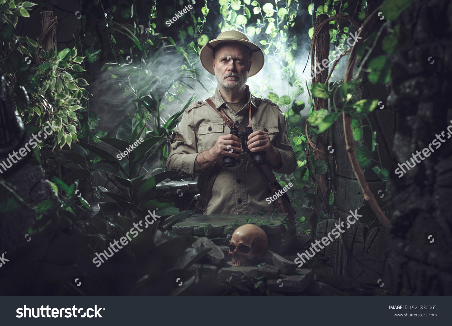 Confident explorer walking in the jungle, he is standing next to ancient ruins and holding binoculars #1921830065