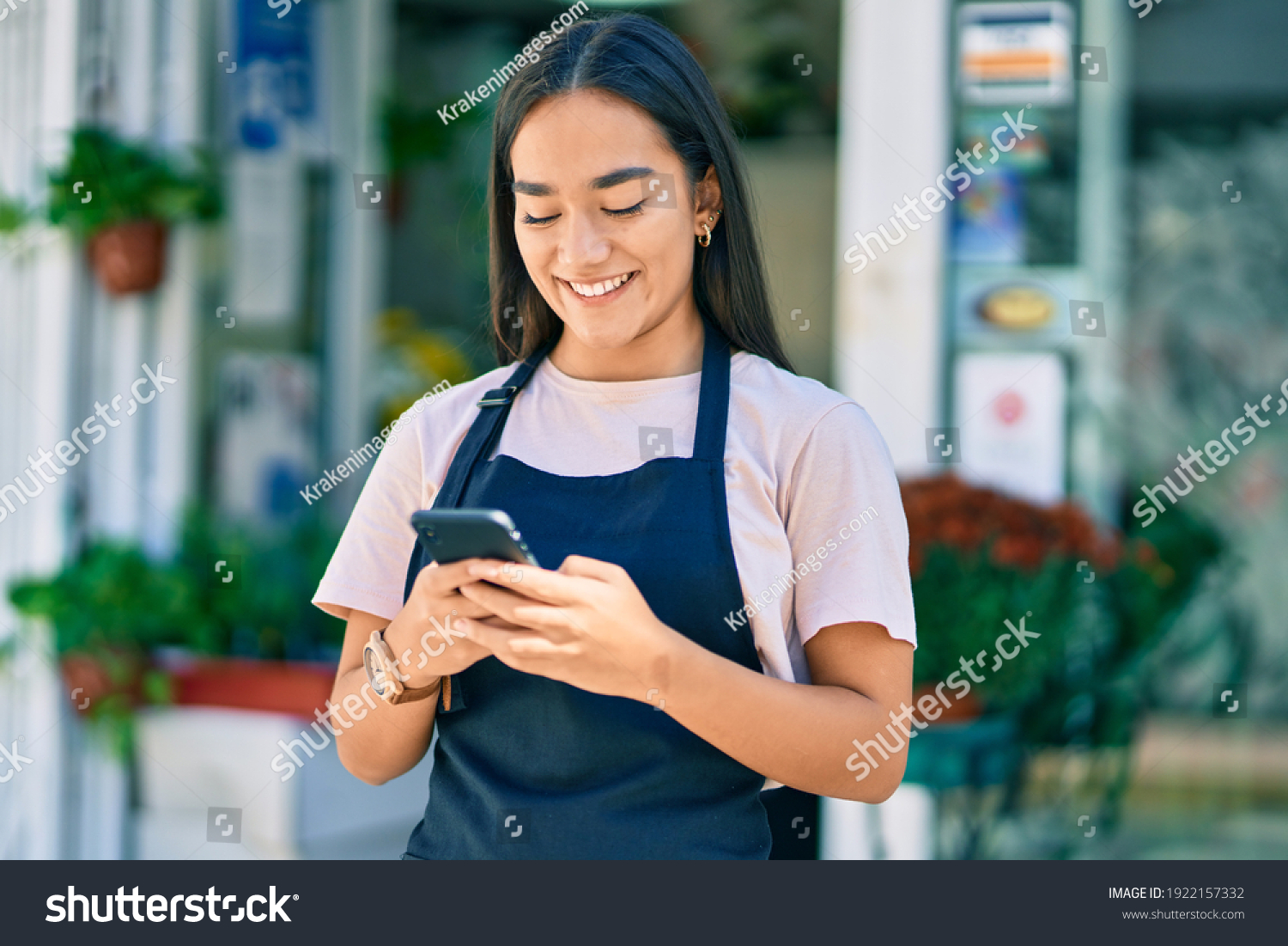 Young latin shopkeeper girl smiling happy using smartphone at florist. #1922157332