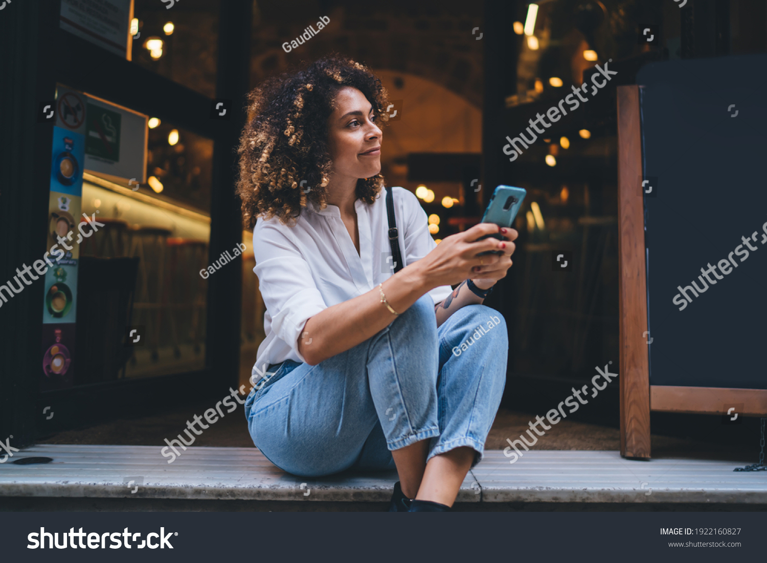 Pretty Caucaisan woman with modern cellphone device in hands resting at touristic street sitting outdoors and smiling, charming hipster girl holding smartphone technology for network and looking away #1922160827