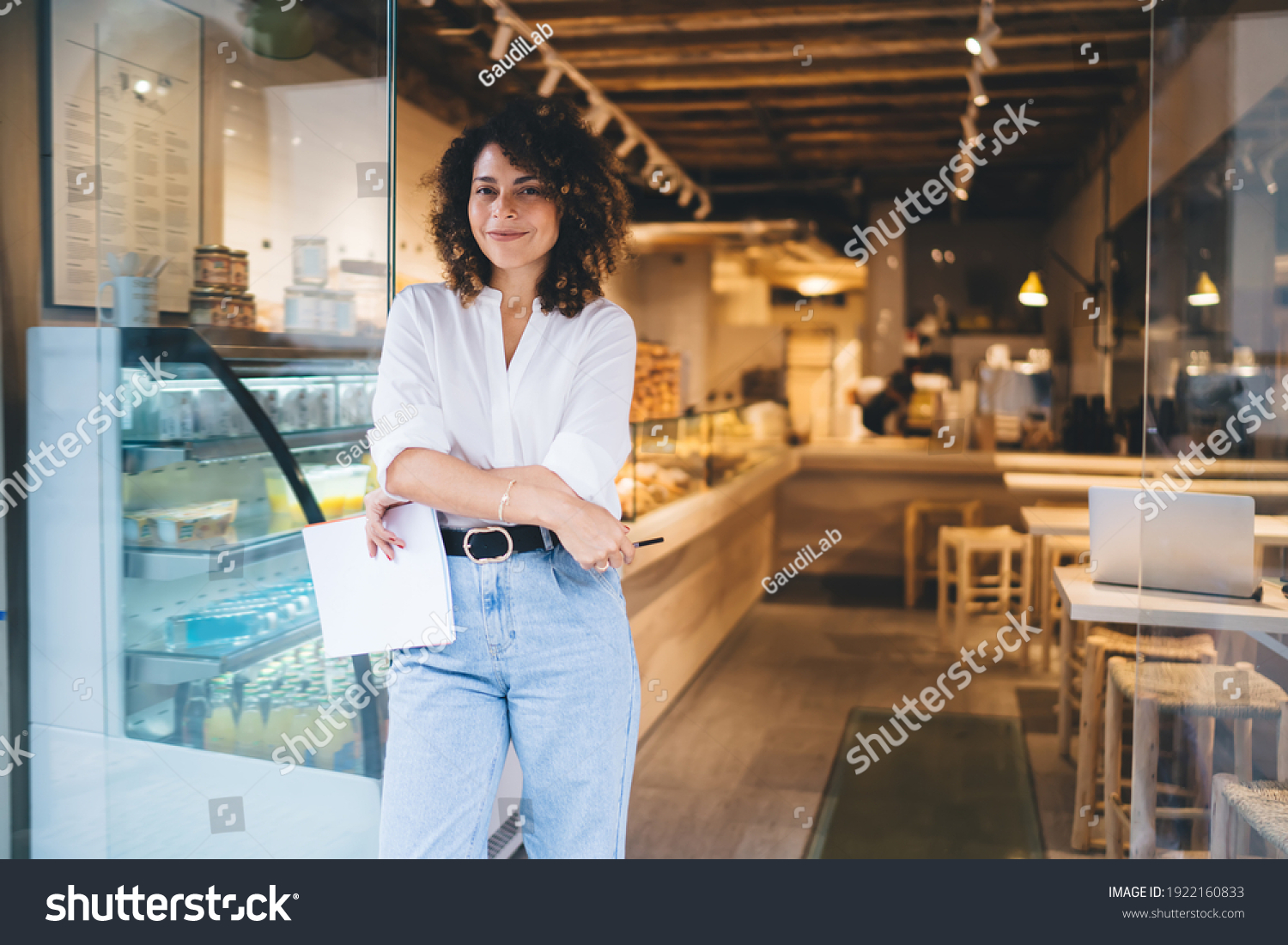 Half length portrait of prosperous manager of local bakery smiling at camera during work day in franchise takeaway cafe, happy woman with paper statistics enjoying time for improve own coffeehouse #1922160833