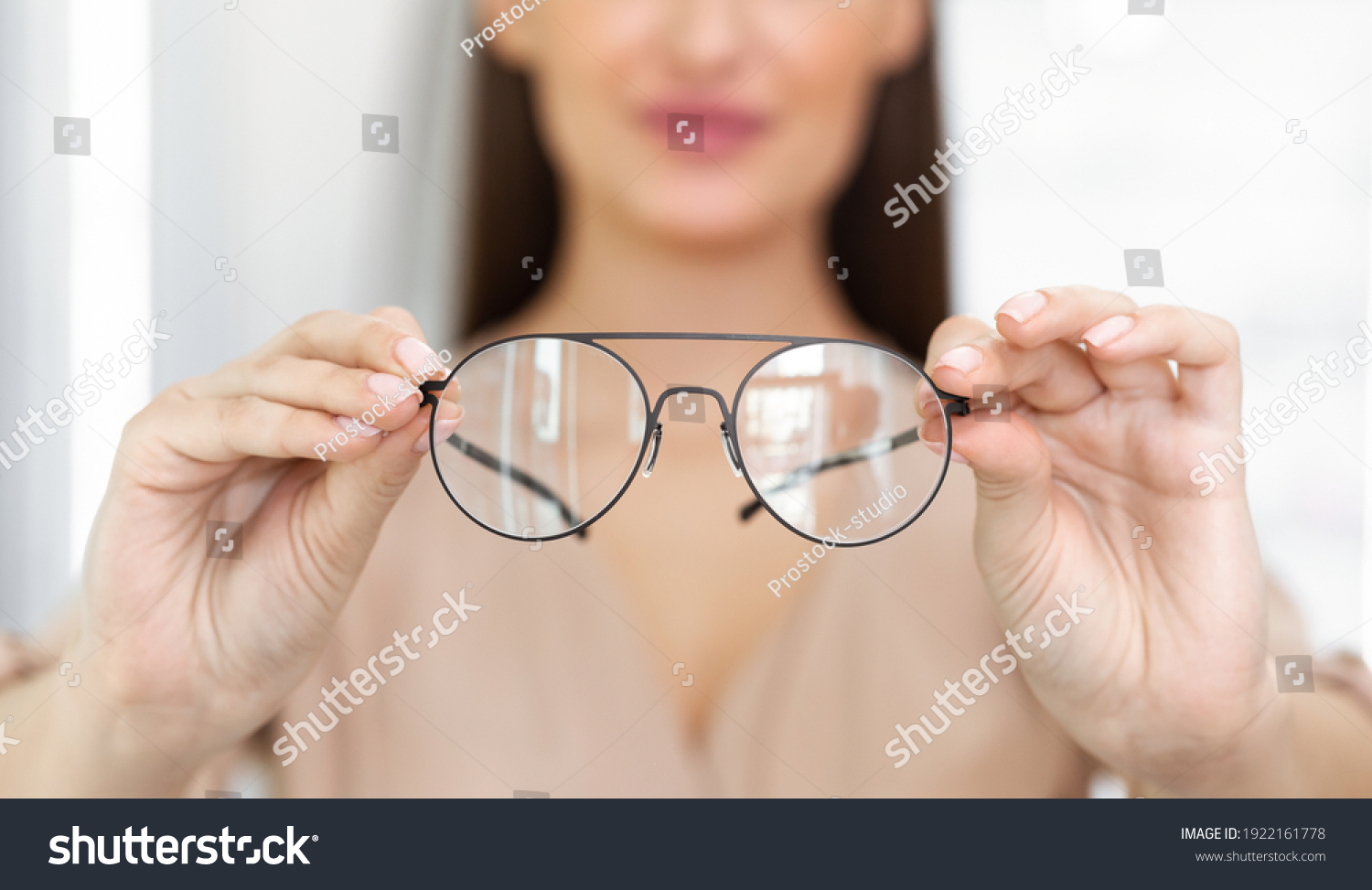 Eyesight And Vision Concept. Closeup of unrecognizable woman showing new eyeglasses to camera, standing at optics store, blurred background, selective focus on eyewear. Lady offering specs #1922161778