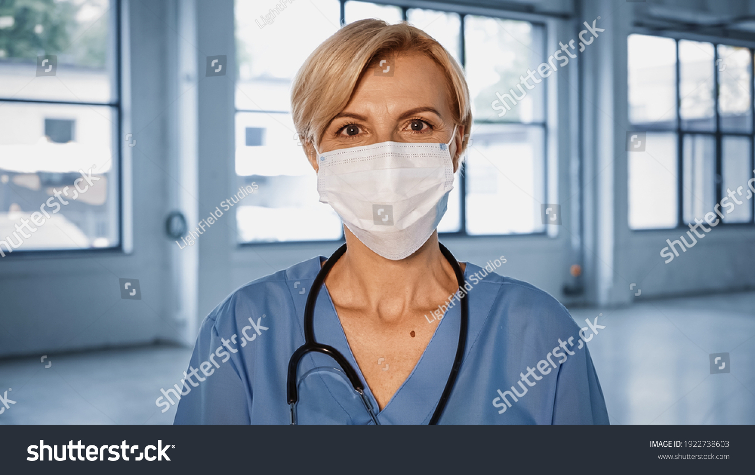 Mature doctor in medical mask looking at camera in hospital #1922738603