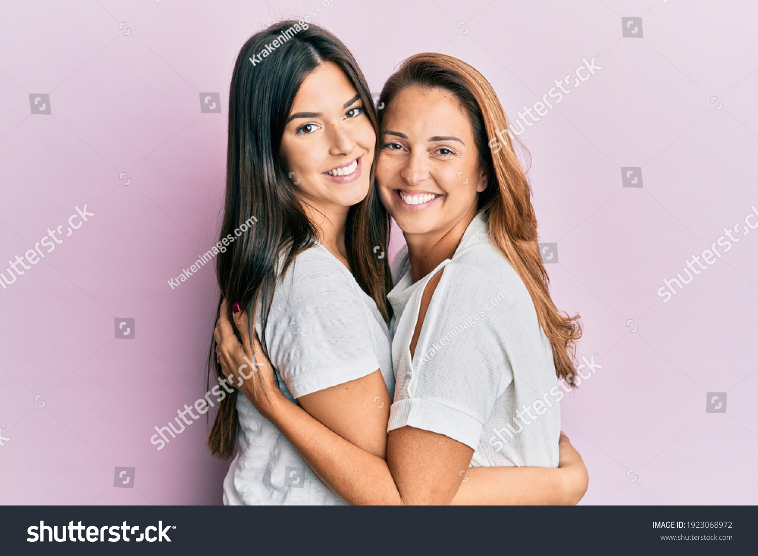 Beautiful hispanic mother and daughter smiling happy hugging over isolated pink background. #1923068972