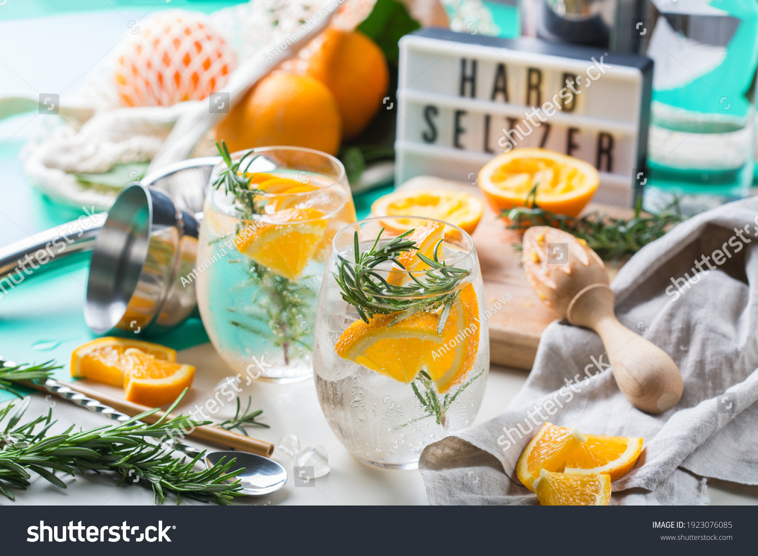 Hard seltzer cocktail with orange, rosemary and ice on a table. Summer refreshing beverage, drink with trendy zero waste accessories, bamboo straw and mesh bag. #1923076085