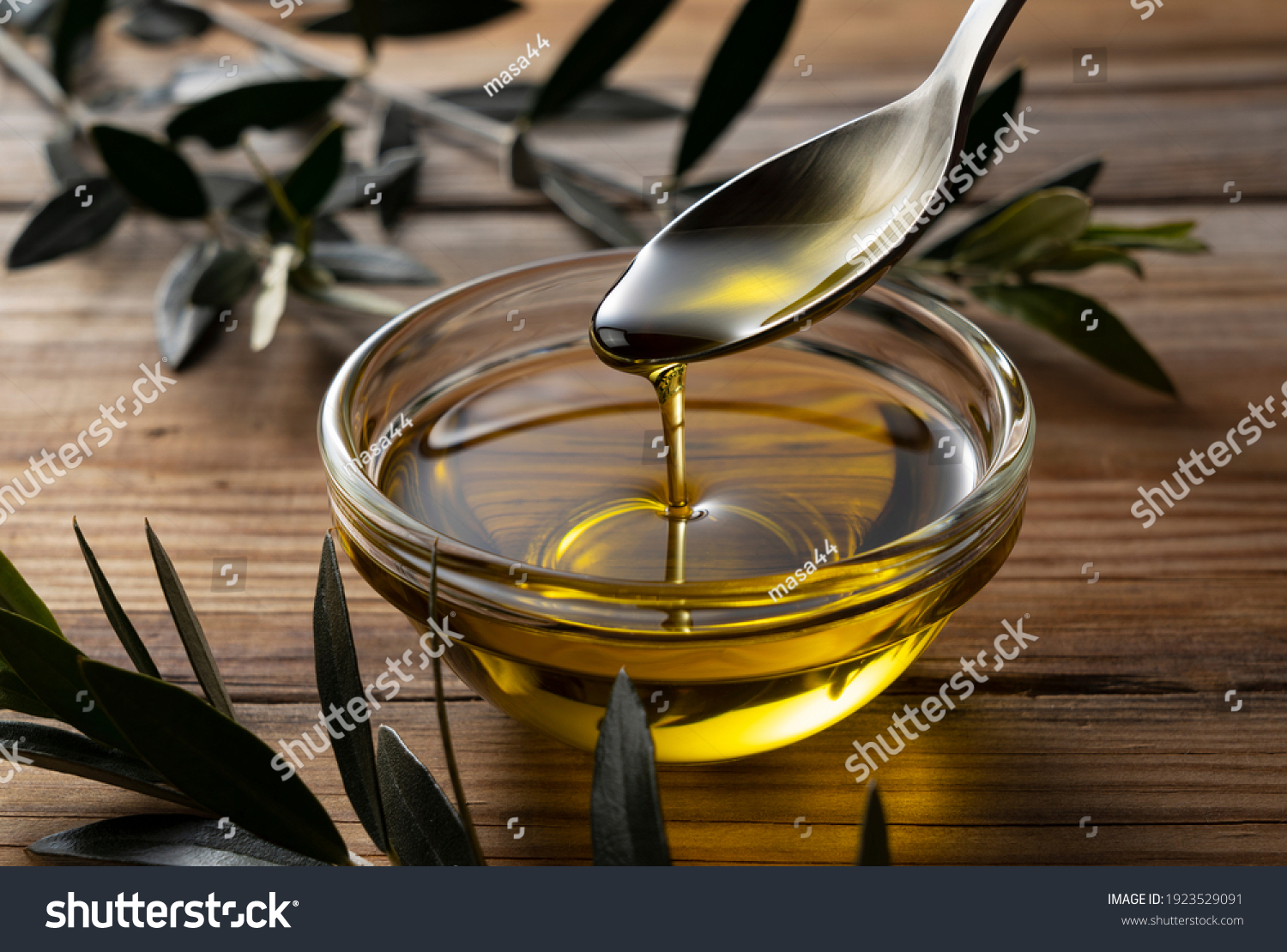 Spooning olive oil into a bowl placed on a wooden background #1923529091