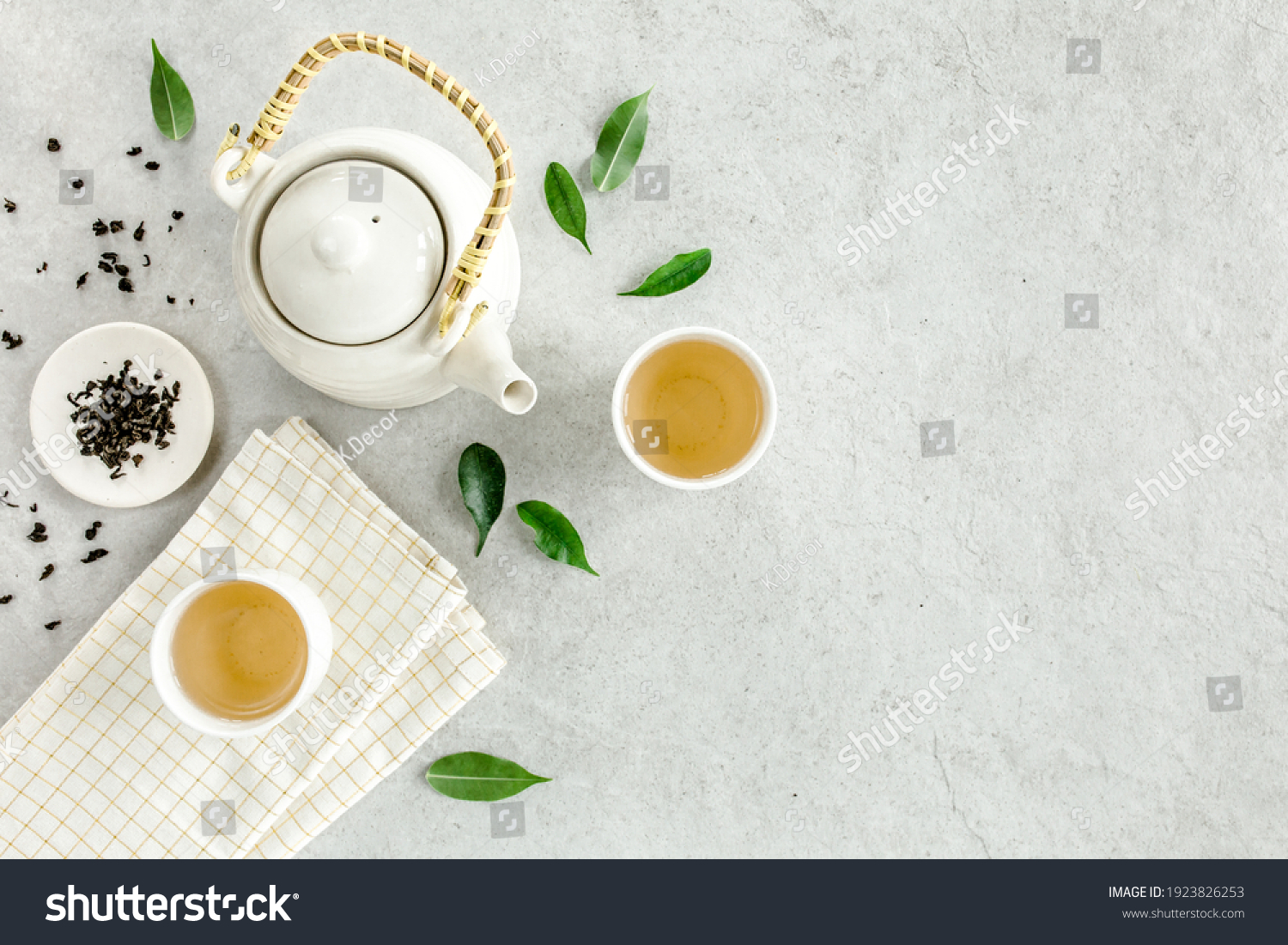 Herbal tea with two white tea cups and teapot, with green tea leaves. Flat lay, top view. Tea concept #1923826253