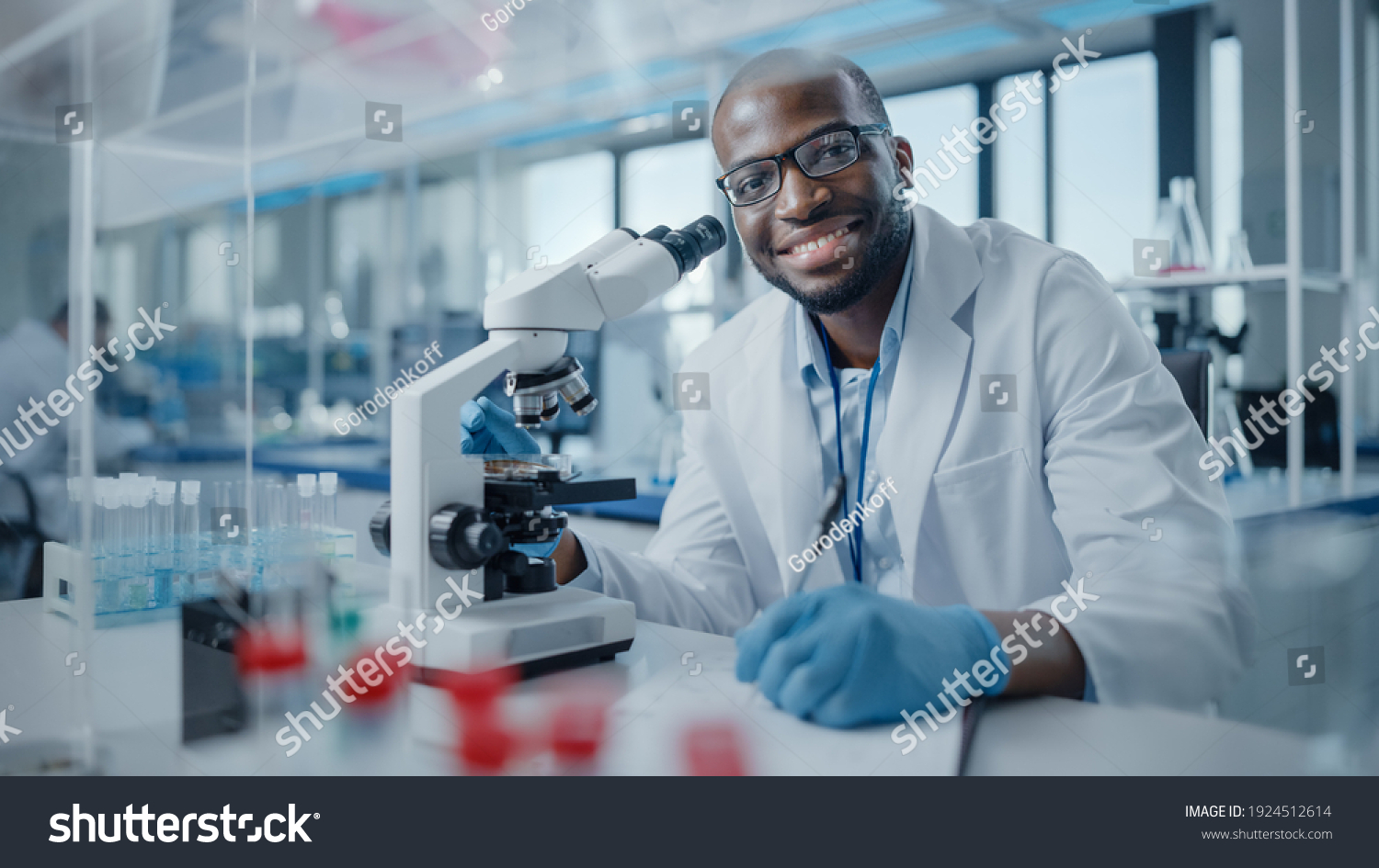 Modern Medical Research Laboratory: Portrait of Male Scientist Using Microscope, Charmingly Smiling on Camera. Advanced Scientific Lab for Medicine, Biotechnology, Microbiology Development #1924512614