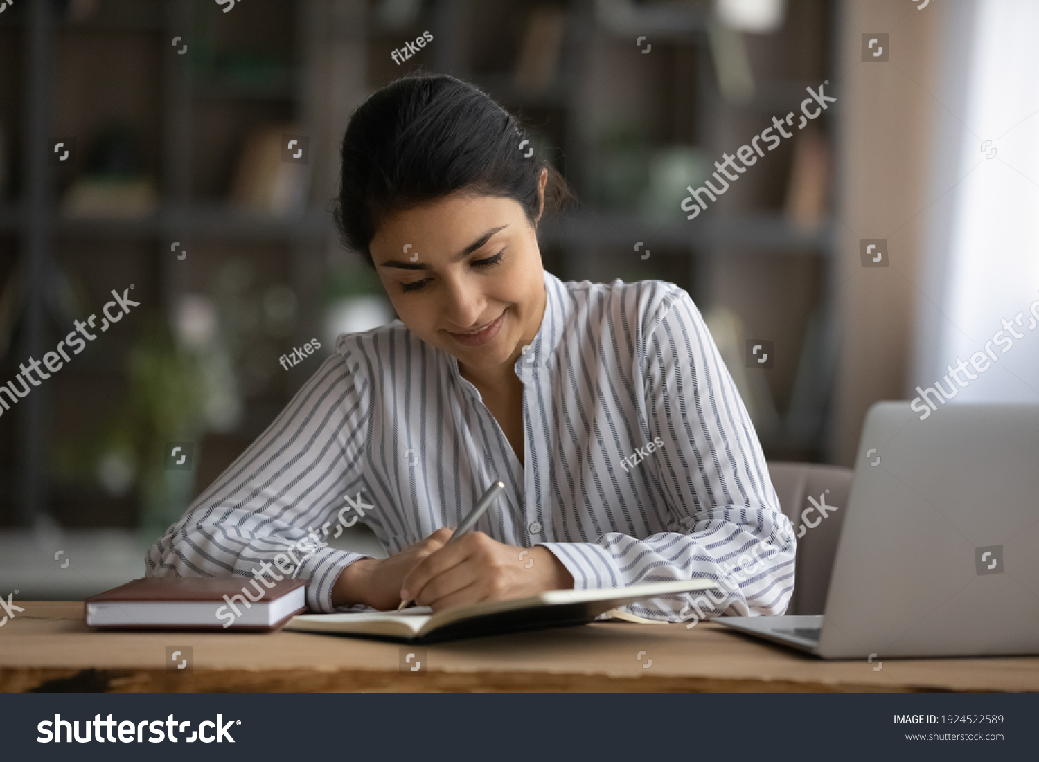 Happy millennial Indian woman sit at desk at home write study online on computer. Smiling young mixed race female work distant on laptop, take course on web. Education, learning concept. #1924522589