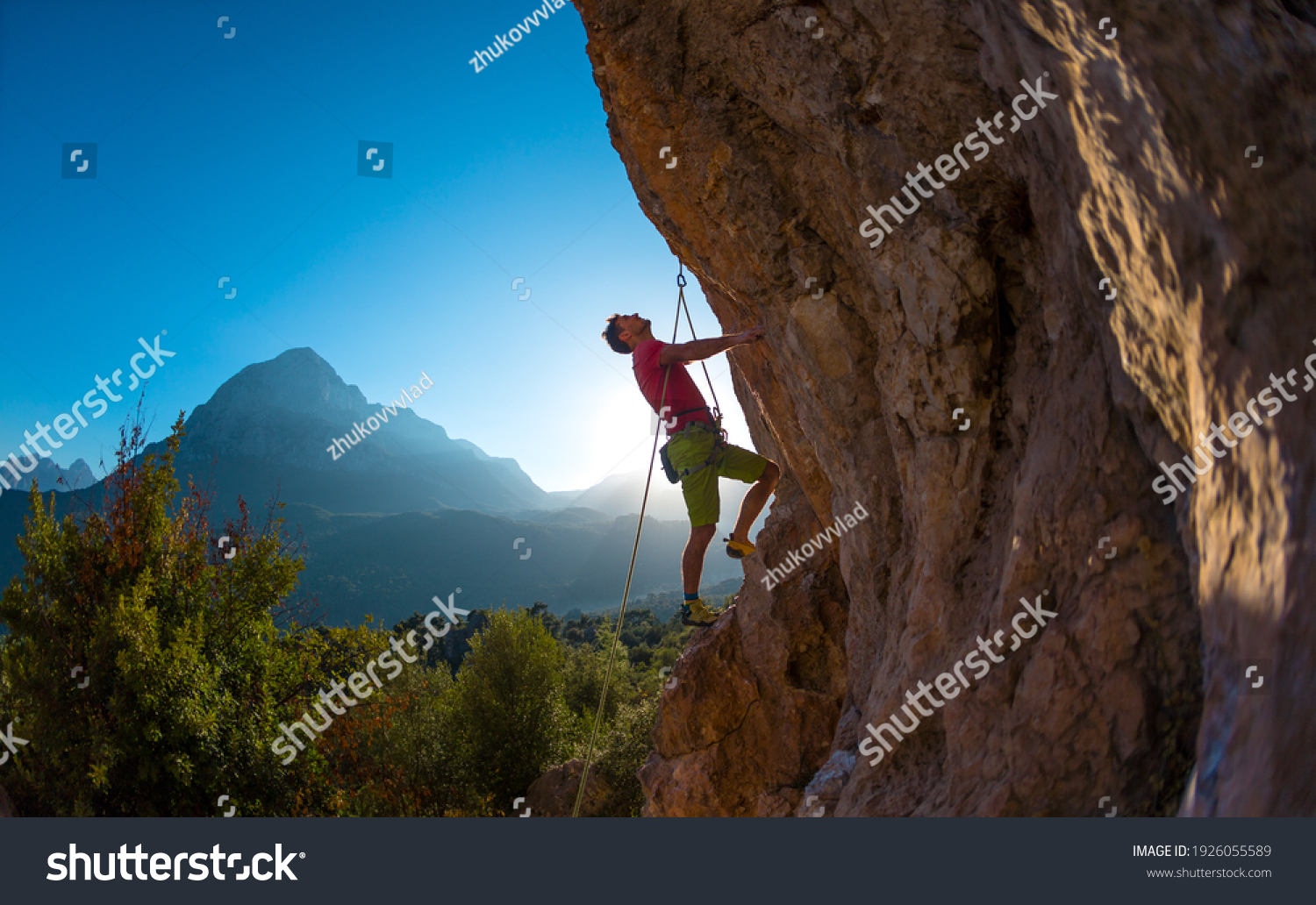 Athletic man climbs an overhanging rock with rope, lead climbing. silhouette of a rock climber on a mountain background. outdoor sports and recreation #1926055589