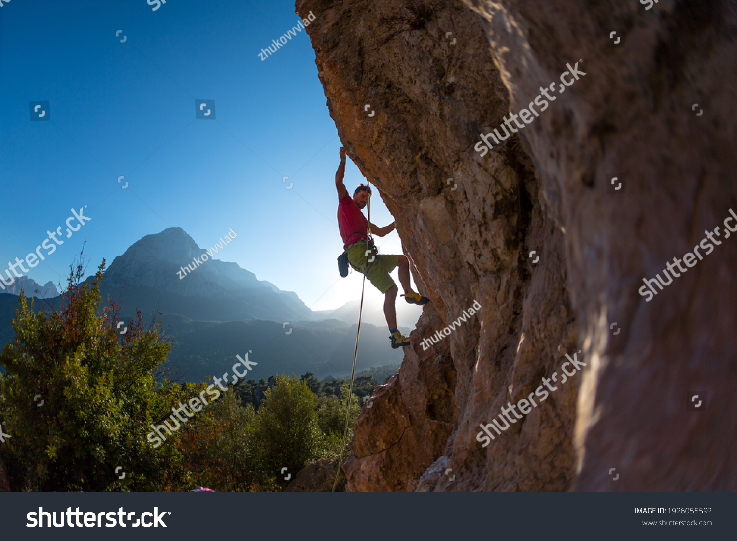 Athletic man climbs an overhanging rock with rope, lead climbing. silhouette of a rock climber on a mountain background. outdoor sports and recreation #1926055592