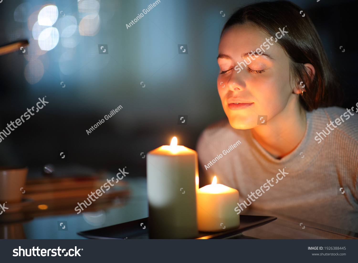 Relaxed woman smelling a lighted scented candle in the night at home #1926388445