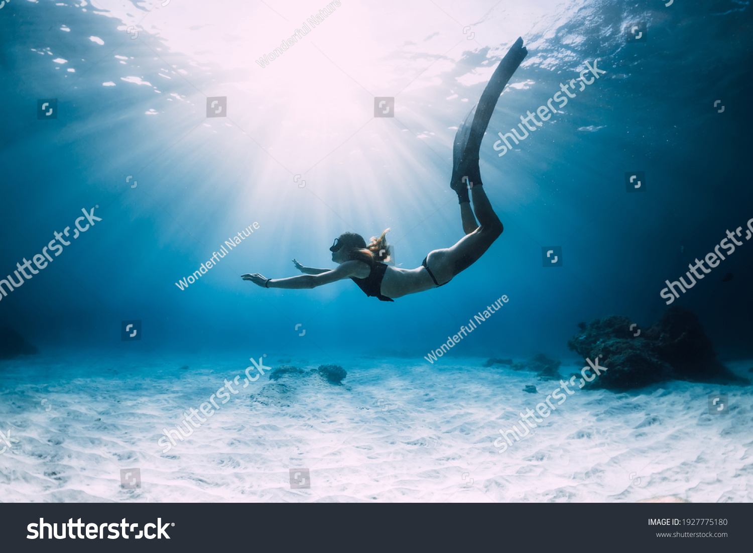 Woman freediver glides with fins. over sandy sea. Freediving and beautiful sunlight in blue ocean #1927775180