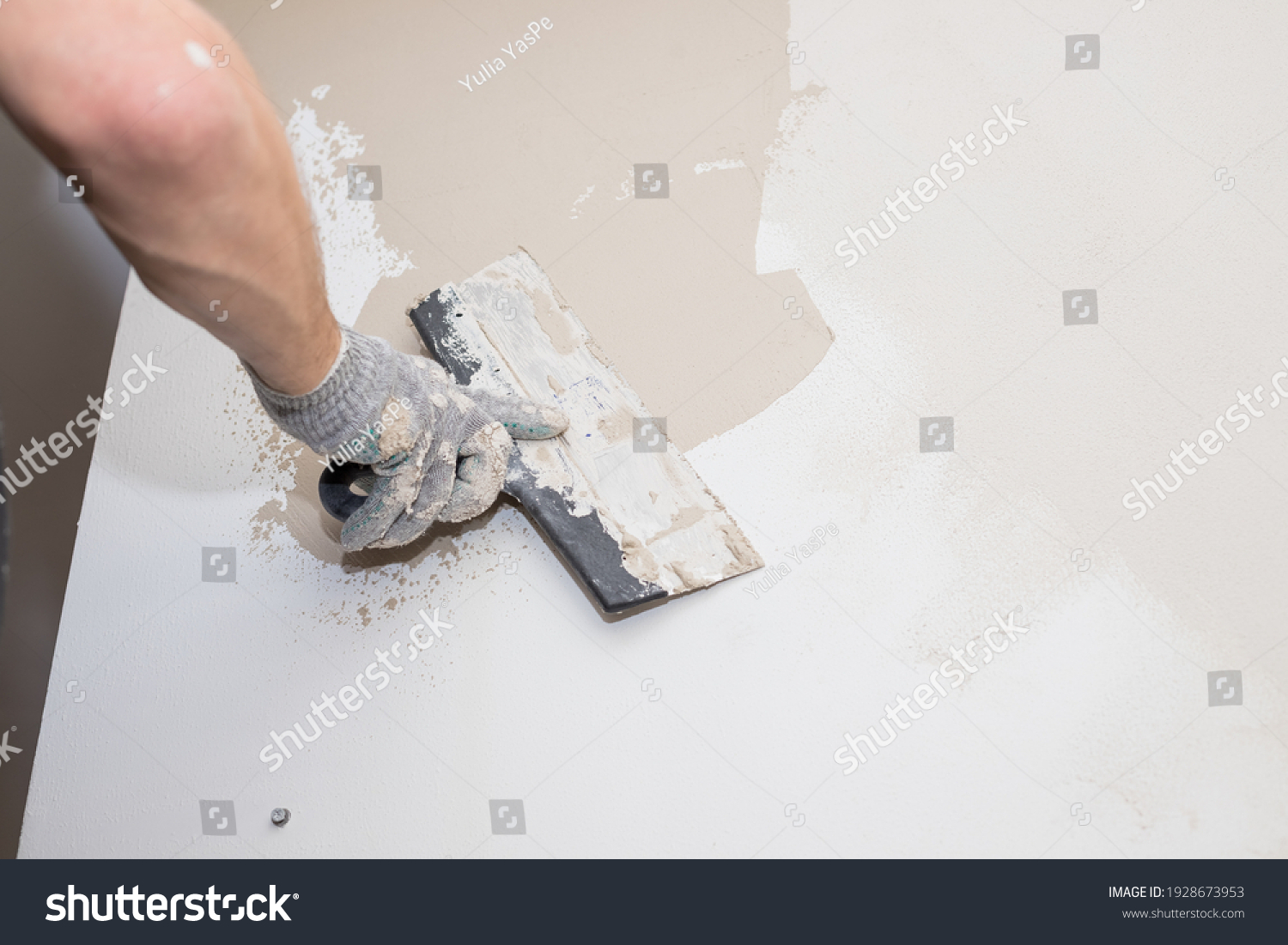hand of builder worker plastering at wall.Renovation workers hand plastering the wall.Construction finishing works.work aligns with a spatula wall.process of applying layer of putty trowel #1928673953