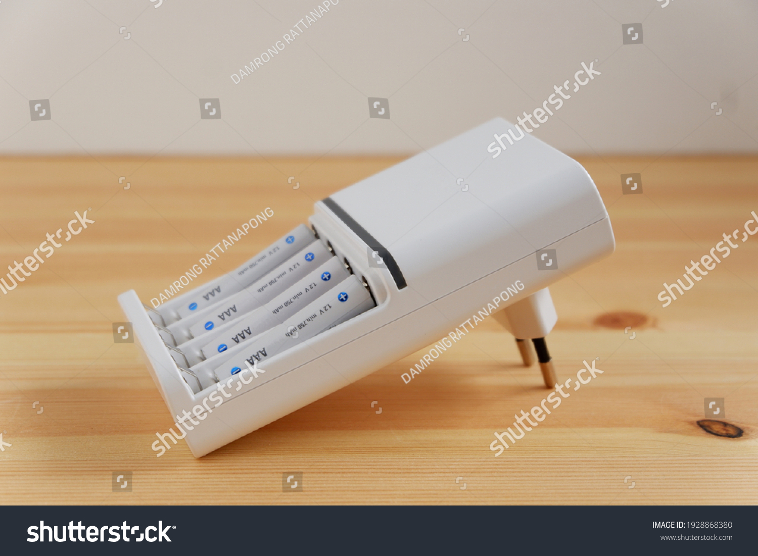 Rechargeable AAA battery in a white charger on wooden background. #1928868380