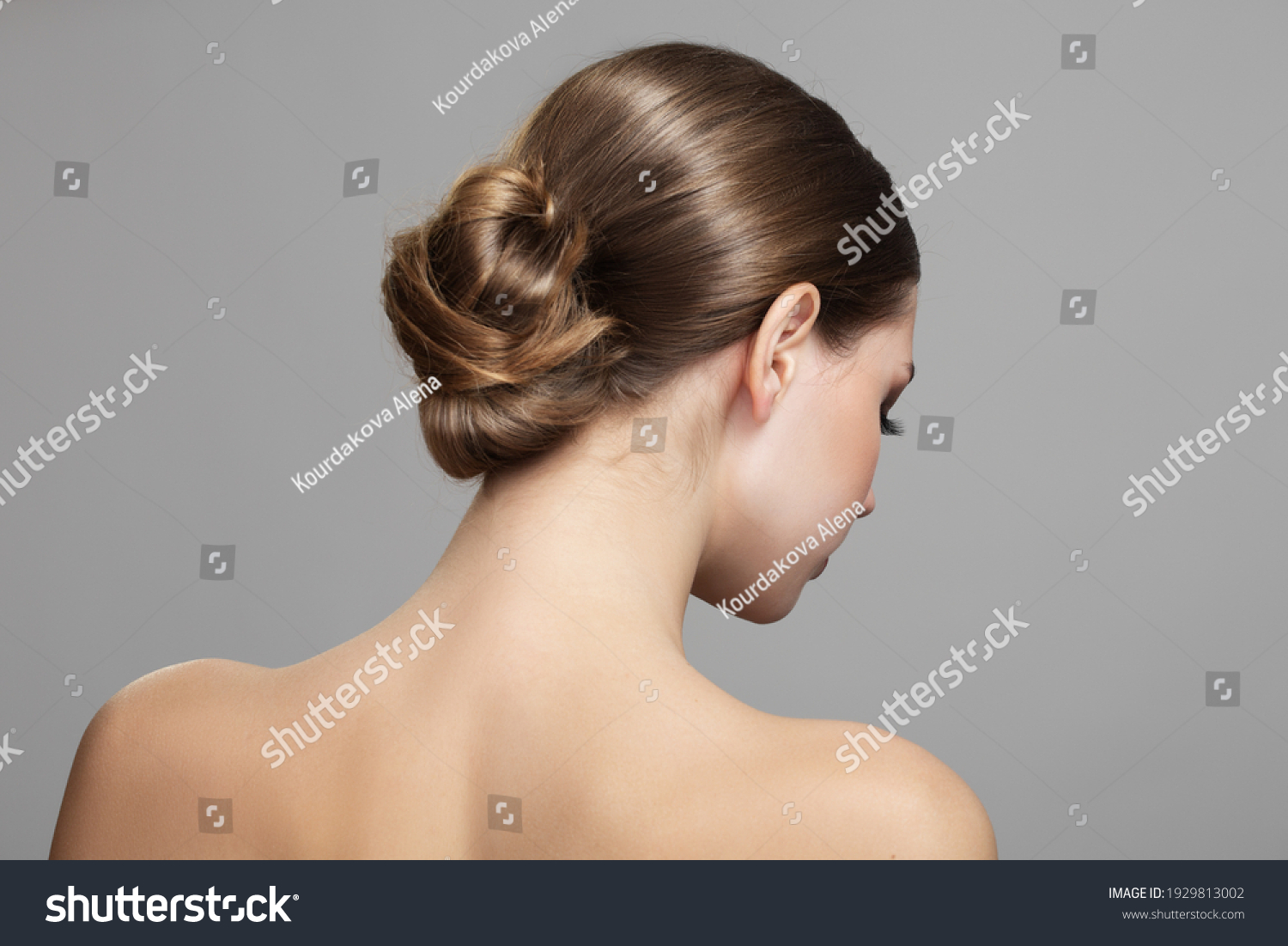 Woman with bun hairstyle on gray background. Bare back, shoulders and neck. Back view #1929813002