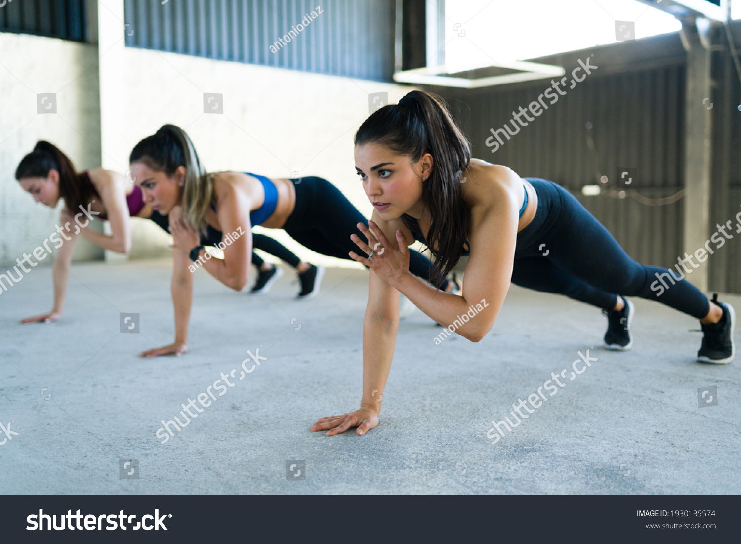 Group of women doing shoulder taps during a high-intensity interval training at the gym. Three fit caucasian women working out with a cardio routine indoors  #1930135574